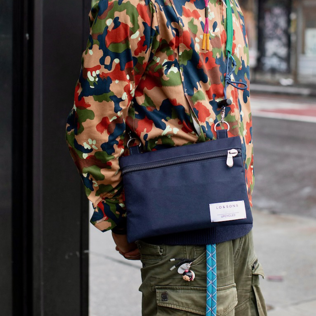 Full color image of Lo & Sons Hilo Flat Pouch being worn by by a model on the streets of NYC